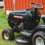 Czarna traktorkosiarka stojąca na trawniku obok czerwonego budynku