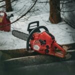 Czerwona pilarka spalinowa leży na ośnieżonych pniach w zimowym lesie