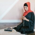 Muzułmanka w chuście modli się na macie z różańcem i Koranem