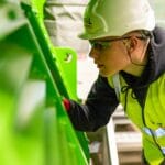 Pracownik fabryki w kasku kontroluje maszynę pod kątem bezpieczeństwa