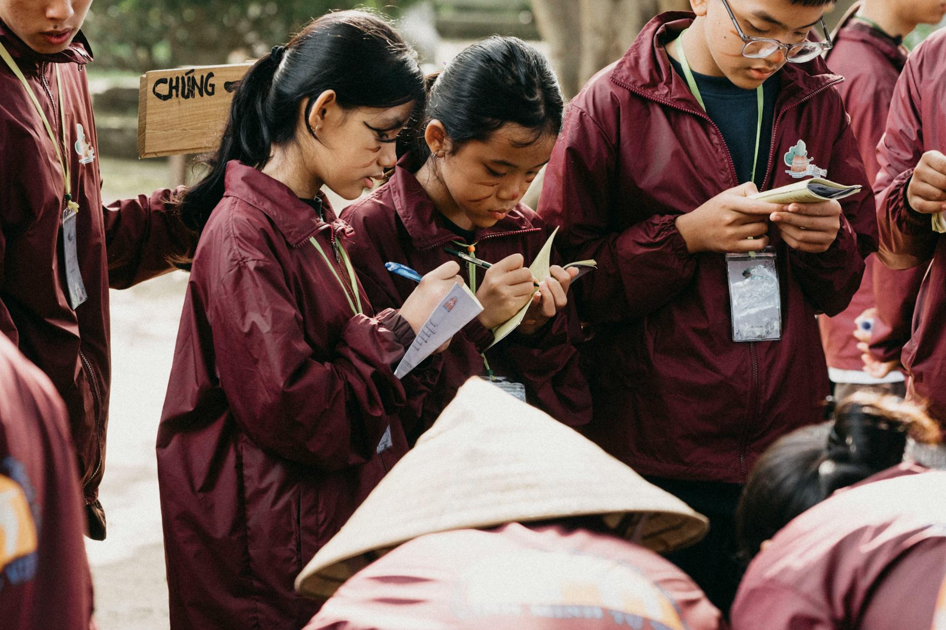 Uczniowie w bordowych mundurkach notują podczas lekcji w terenie