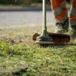 Pracownik przycina trawę wykaszarką przy drodze
