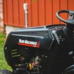 Traktorek ogrodowy Yard Machines na trawie obok czerwonego schowka