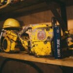 Stare pilarki spalinowe i kask ochronny na drewnianej półce w warsztacie