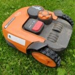 Pomarańczowa kosiarka automatyczna na zielonym trawniku w ogrodzie